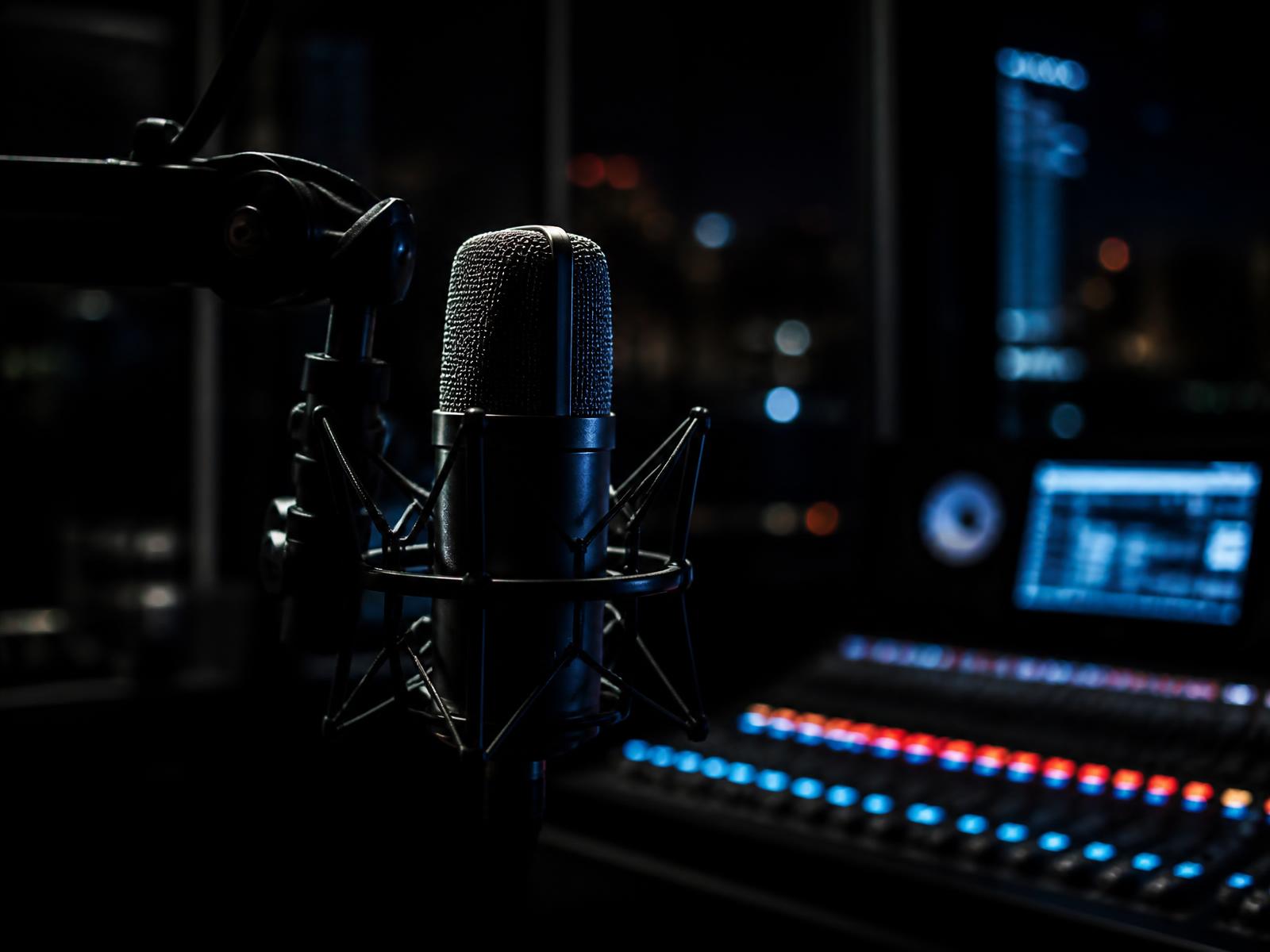 Studio microphone lit in blue and red in front of a mixing desk